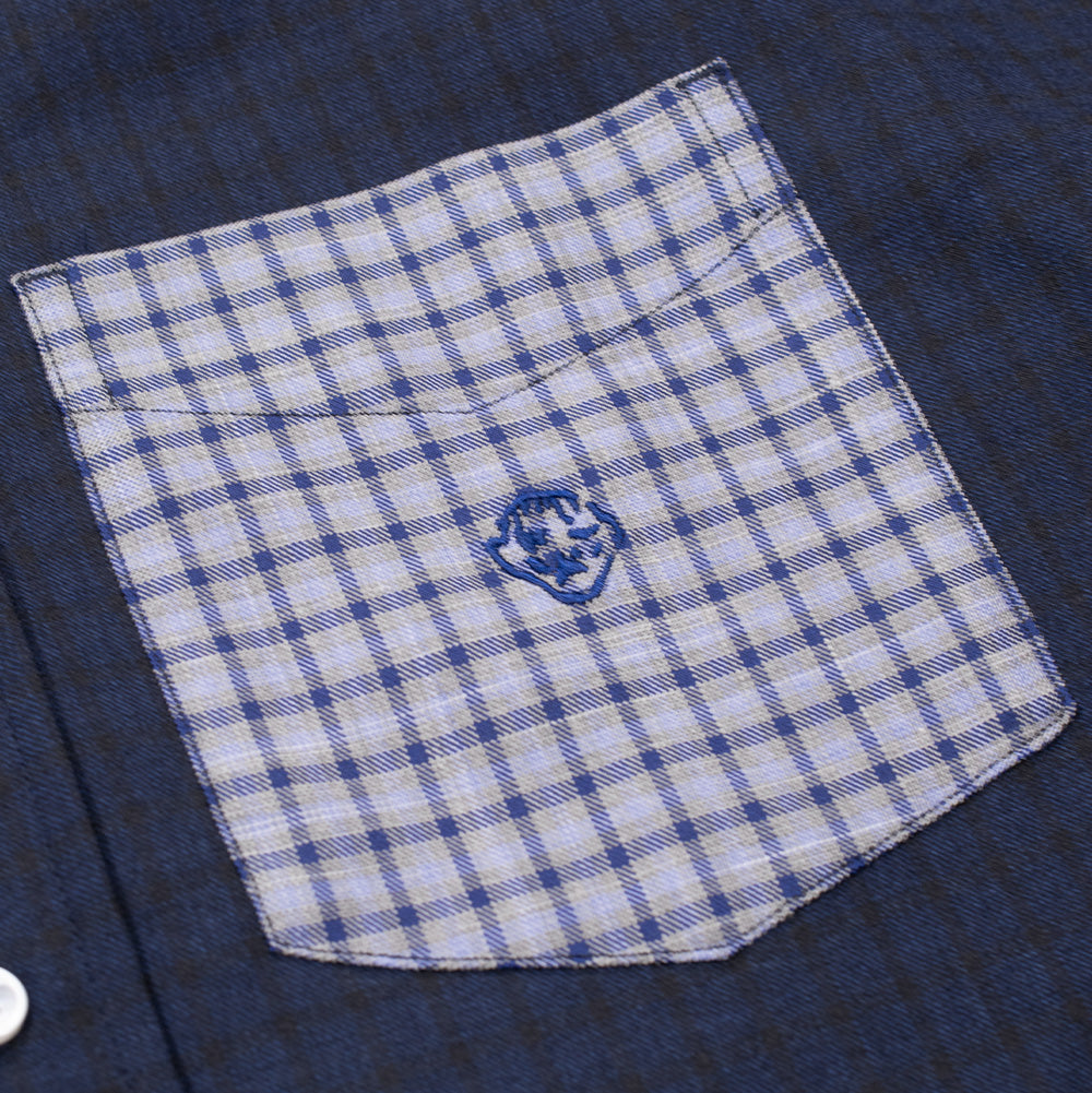 Detailed close-up shot of the left chest pocket on the Dancer Split Checked Shirt, focusing on the light blue gingham check patch pocket stitched against the dark navy woven cotton body, detailed with Dancer's signature abstract doodle logo embroidered in royal blue thread.