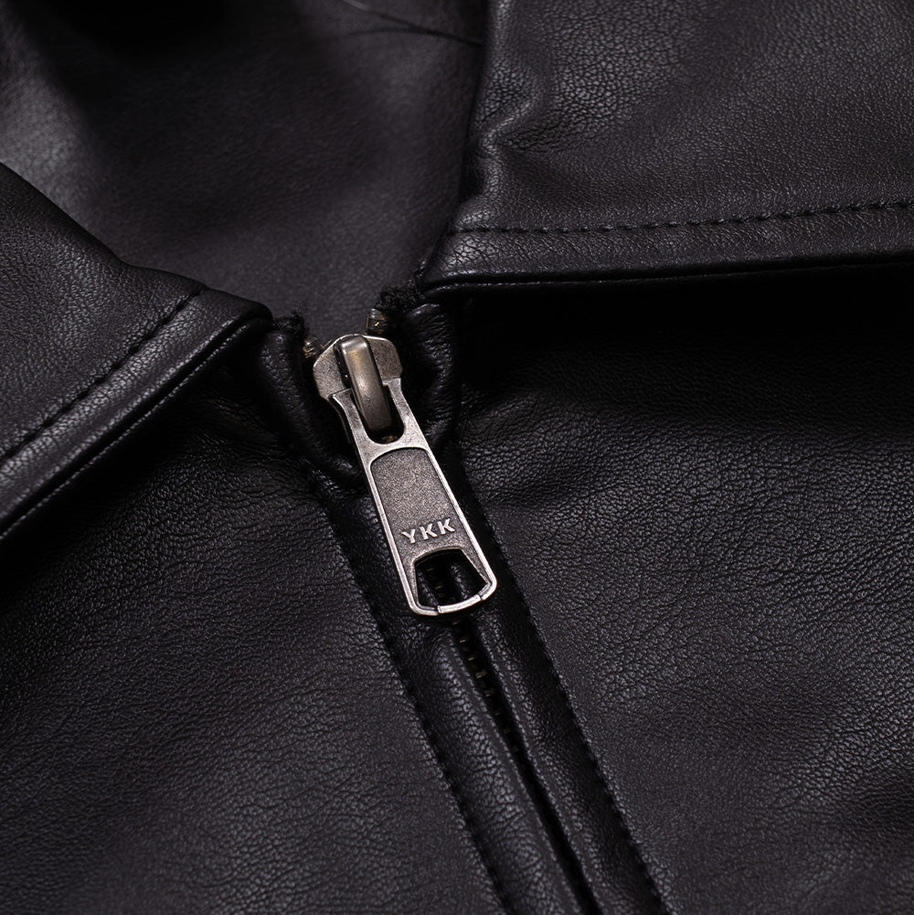 Macro studio view of the front zipper closure on the Huf X Three 6 Mafia jacket, detailing the antique silver metallic YKK zipper pull, folded faux leather collar, and durable topstitching along the black leather placket.