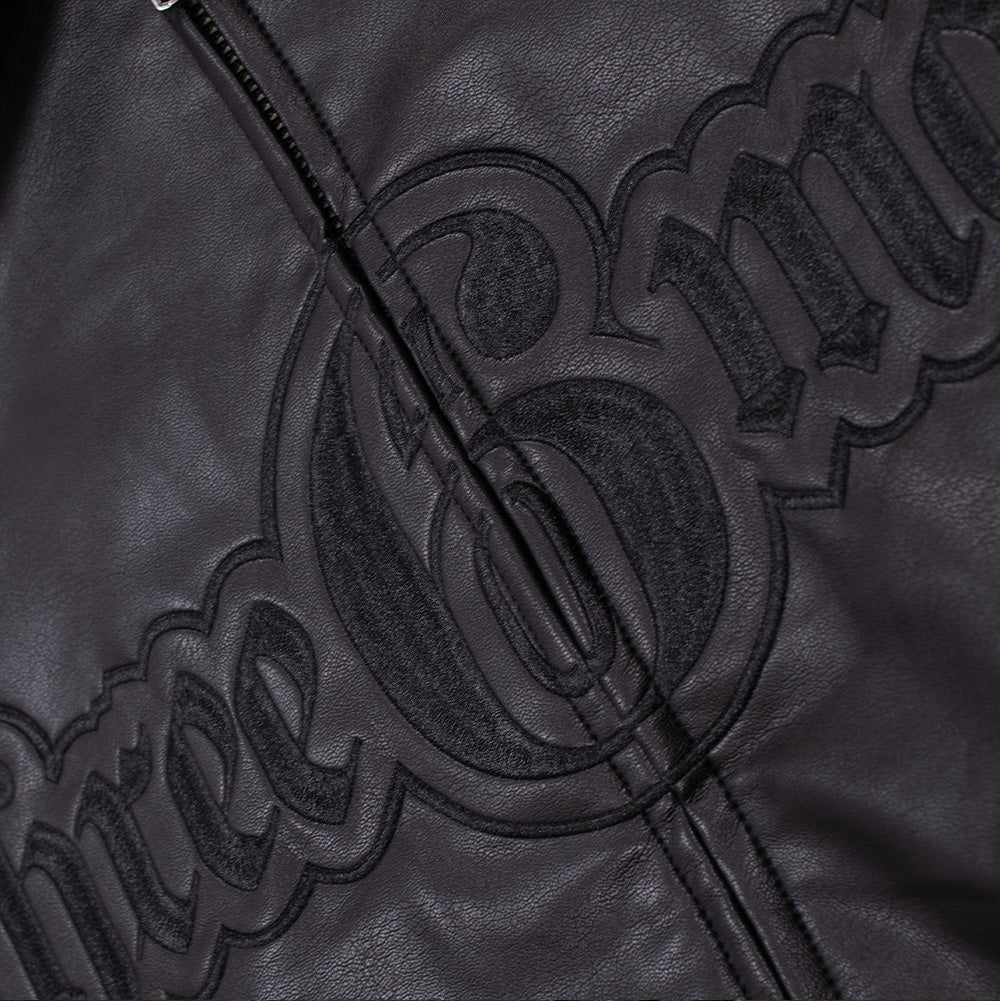 Close-up shot of the front chest embroidery on the Huf X Three 6 Mafia jacket, showing the textured black tackle-twill and dense edge stitching of the split Three 6 Mafia logo across the center zipper seam.