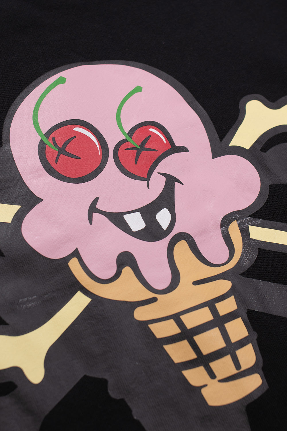 Close-up of IceCream Cone & Bones chest graphic showing vibrant cherries, pink ice-cream scoop, and crossbones print on black cotton crewneck, highlighting IceCream’s bold skate-inspired streetwear aesthetic.