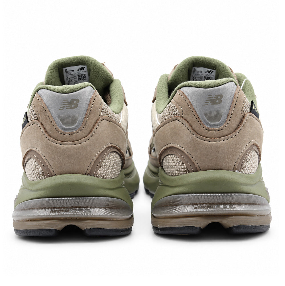 Rear studio view of the heel counters on the New Balance 2010 GORE-TEX in Mushroom Timberwolf, showing the reflective silver triangular heel tabs printed with the NB logo, multi-layered tan nubuck panels with woven underlays, soft olive fleece collar trim, and sculpted olive green midsole debossed with ABZORB SBS branding above the durable rubber outsole.