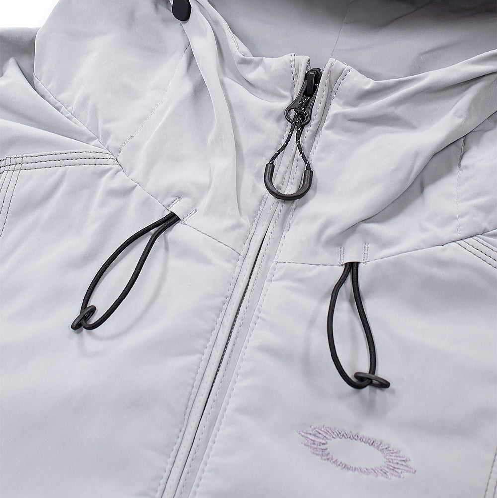 Macro studio close-up of the neckline and hood on the Oakley FGL Sector Jacket, detailing the matte black metal zipper puller with ergonomic cord loop, two-point bungee cinch cords with plastic toggle locks, tonal embroidered Oakley scratch logo on the upper chest, and precision multi-needle stitching on the soft-touch grey technical shell.