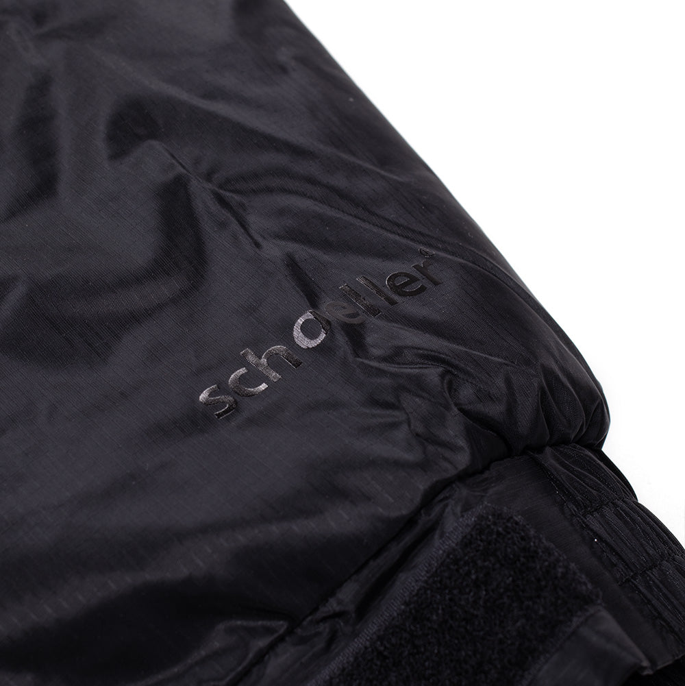 Macro perspective of the sleeve cuff on the Oakley FGL Stealth Ins Jacket 2.0, capturing the tonal black embroidered "schoeller" technical fabric logo positioned above the gathered elasticated wrist and velcro adjustment strap.