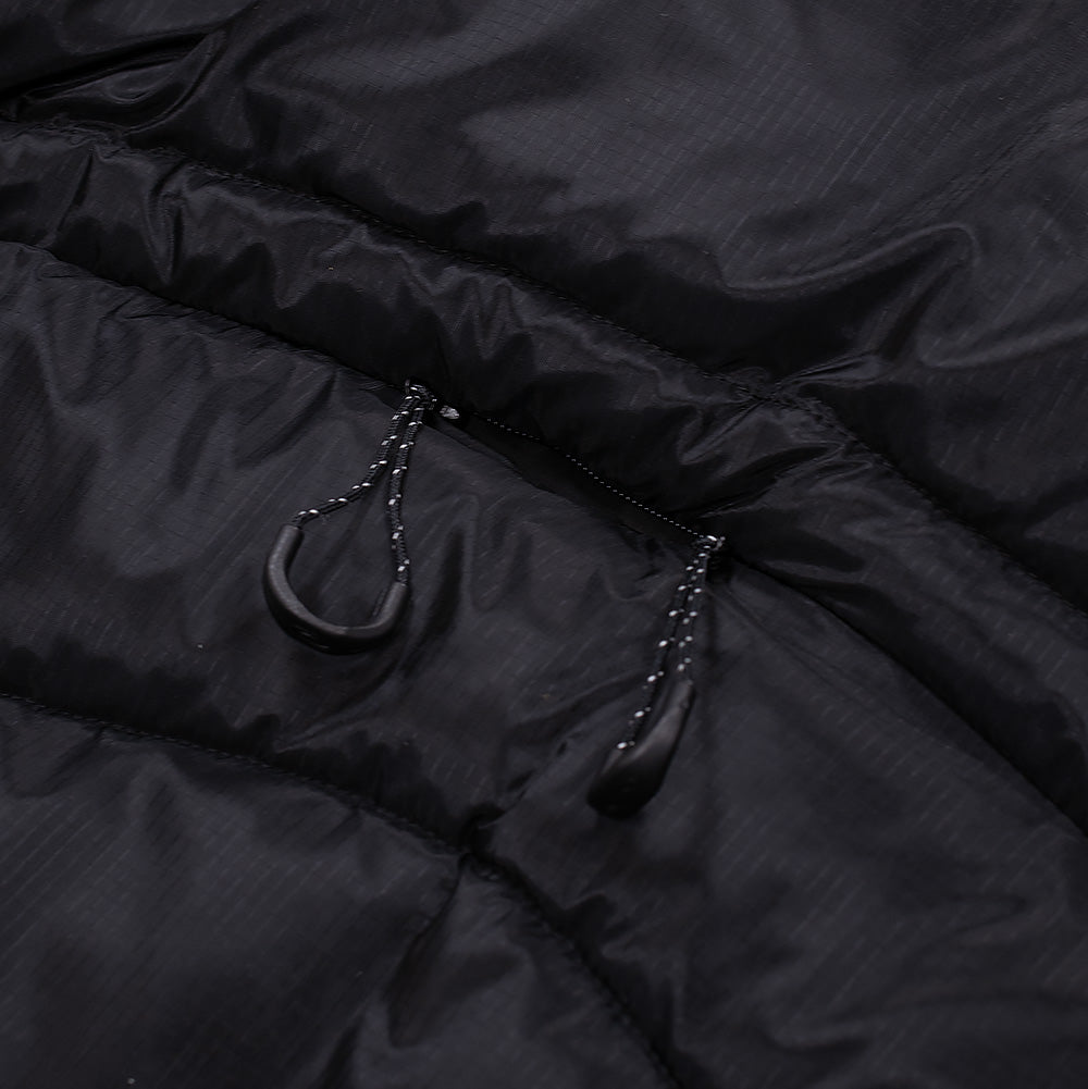 Detailed macro view of the rear waist cargo pocket on the black Oakley FGL Stealth Ins Jacket 2.0, highlighting the horizontal quilted seam, concealed zipper track, and dual utility paracord pullers with contoured matte black grips.