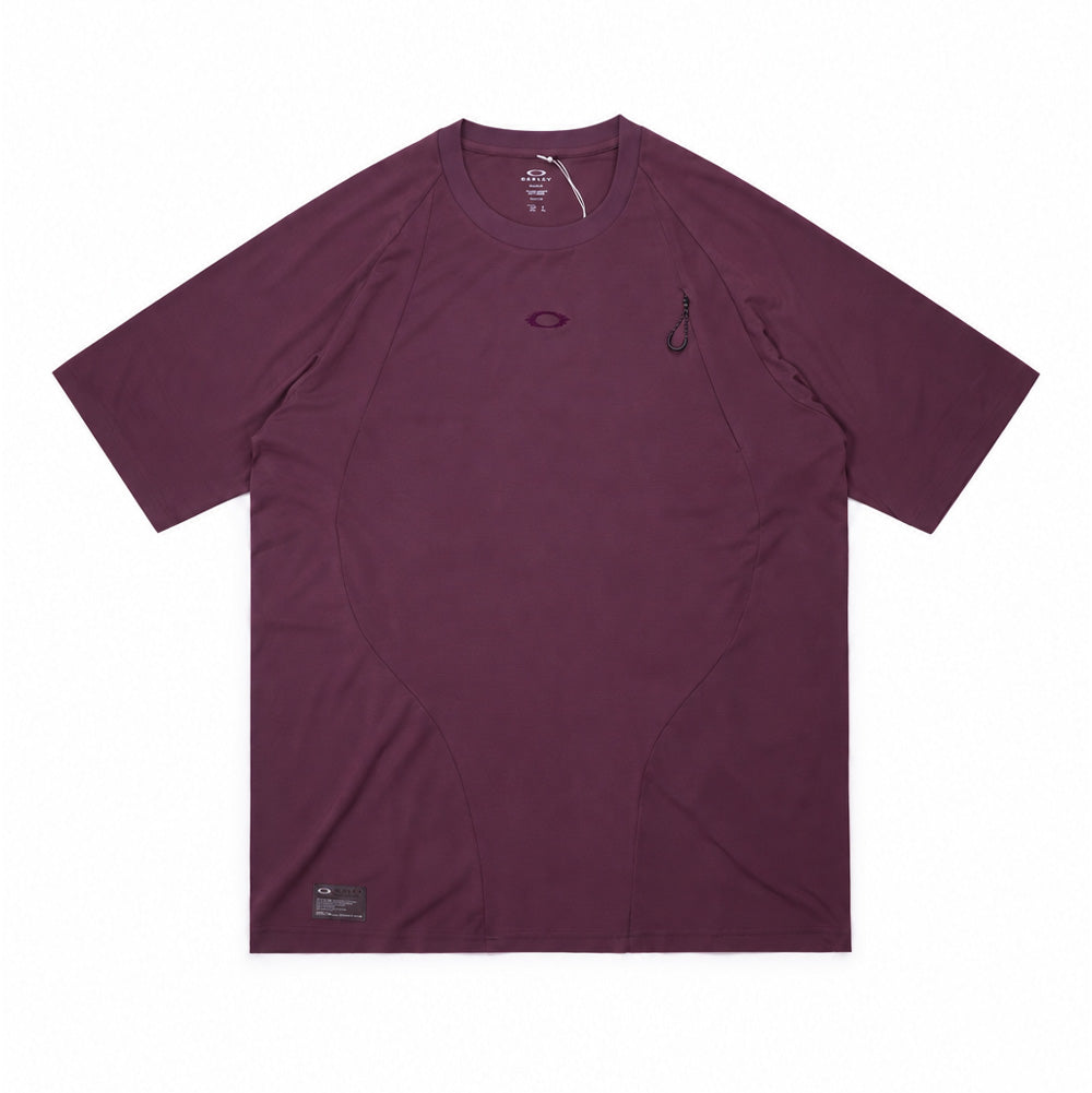 Front flat lay studio view of the Oakley FGL Union Short Sleeve Tee 6.7 in Rouge, showcasing an outdoor technical performance t-shirt in deep plum purple, featuring ergonomic curved seam construction, ribbed crewneck collar, tonal embroidered chest logo, a concealed vertical chest zipper pocket with a textured pull loop, and a dark rectangular Oakley FGL spec label at the bottom right hem.