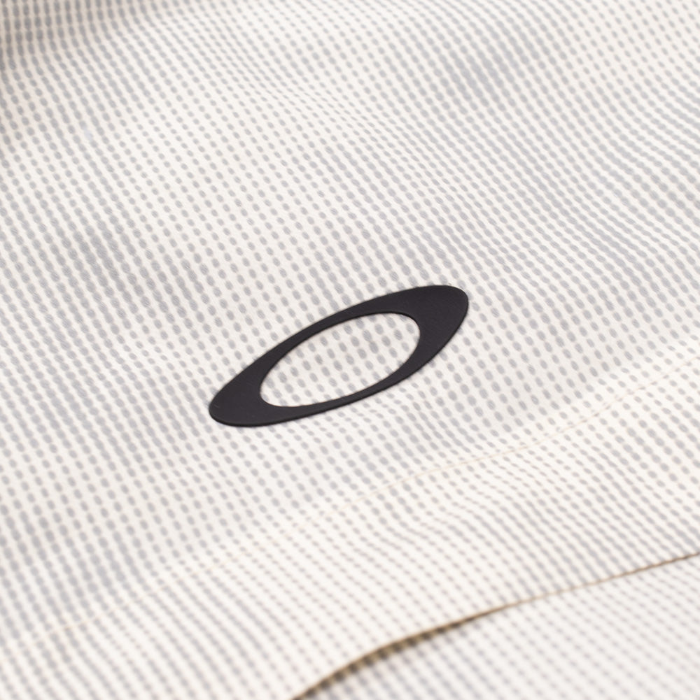 Detailed macro perspective of the chest logo on the Oakley Mthod Glow Shell Jacket, highlighting the matte black rubberized Oakley Ellipse icon heat-transferred cleanly over the water-resistant micro-perforated grid shell material.