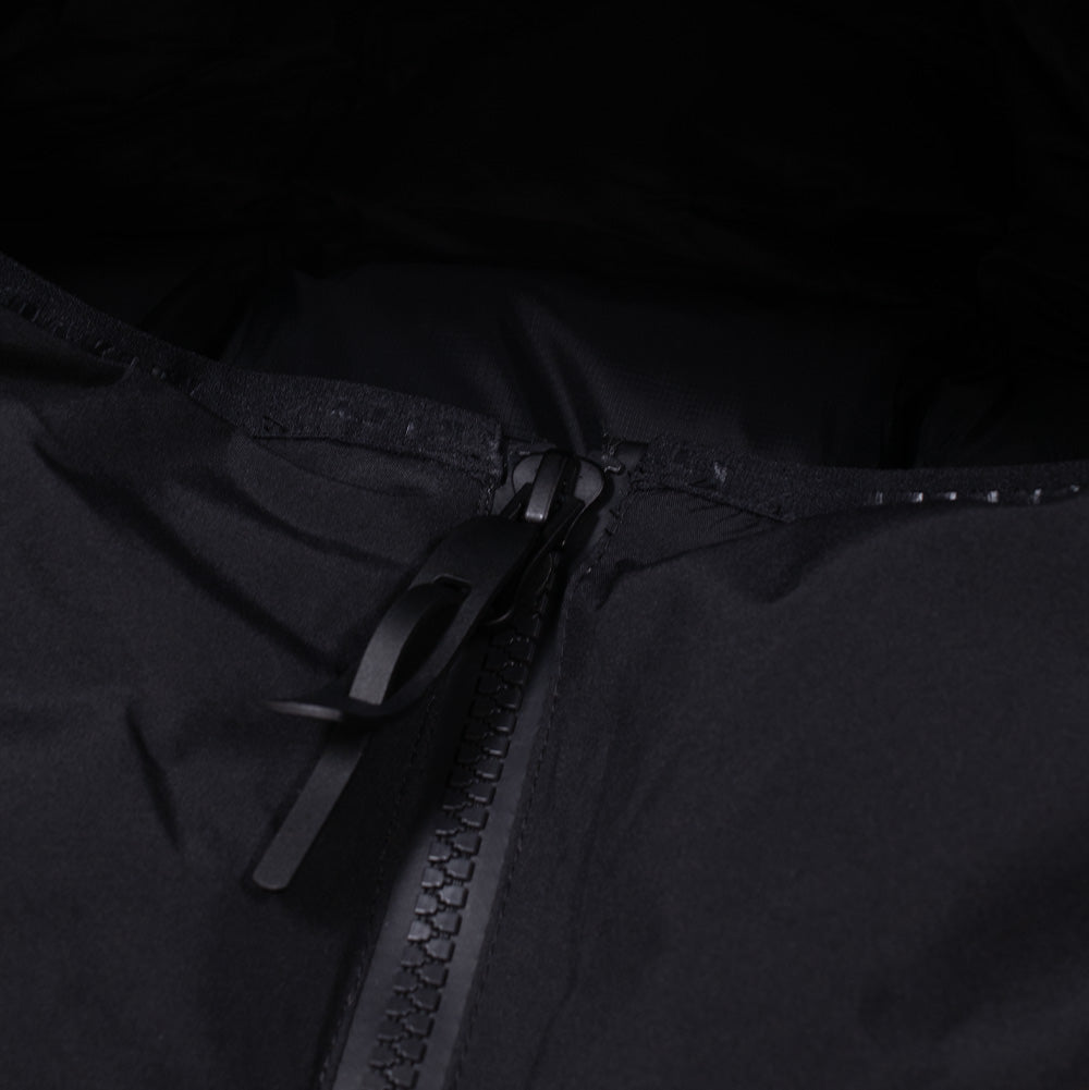 Macro studio close-up of the upper front zipper and chin guard on the Oakley Retrofuel Gore-Tex Down Jacket, detailing the rugged black Vislon AquaGuard teeth, matte black metal slider with an ergonomic pull loop, and weather-sealed storm flap backing in pitch black technical fabric.