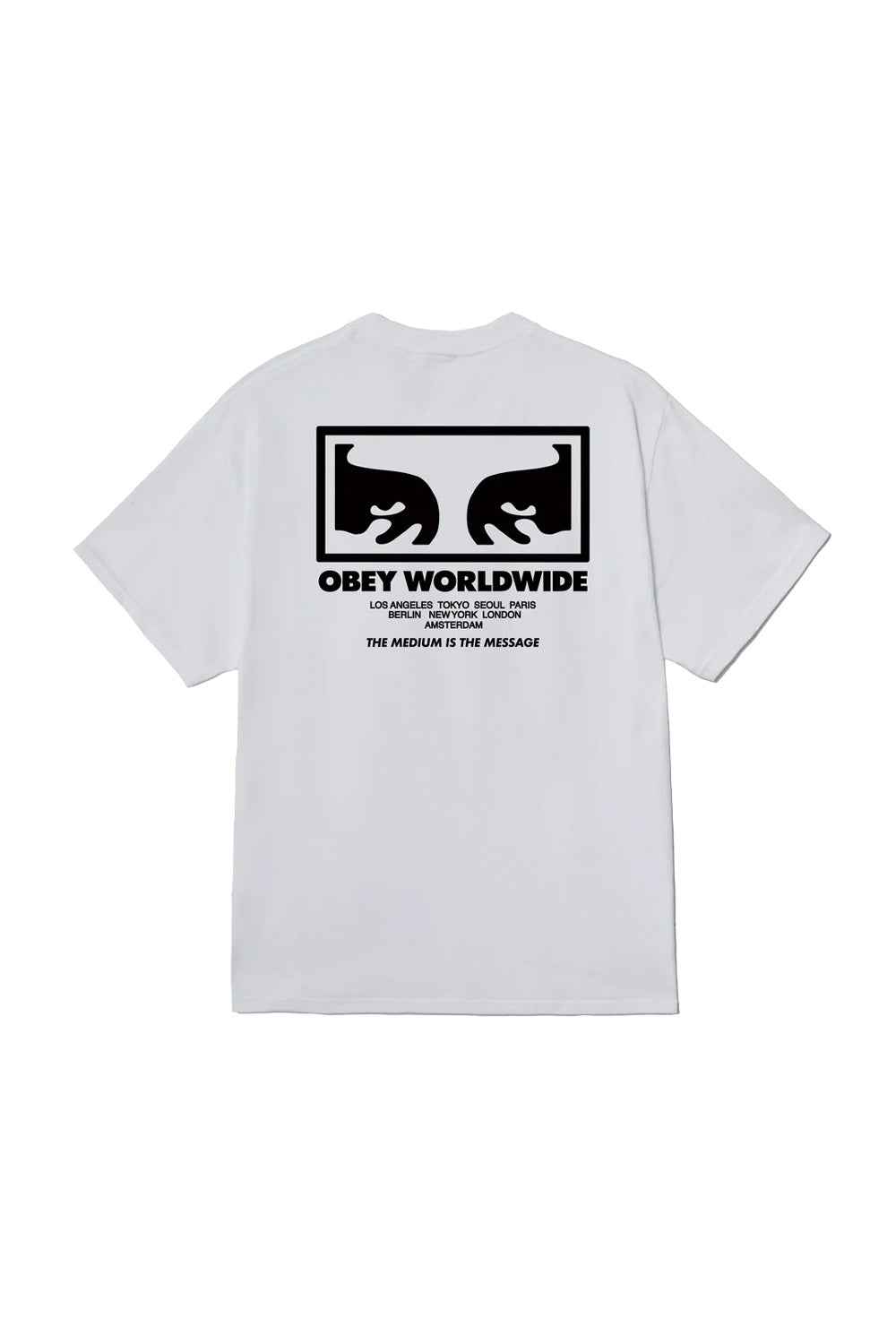 Back view of the white Obey The Medium Is The Message T-Shirt, crafted from 100% cotton jersey, featuring a bold black screen-printed Shepard Fairey Giant Eyes box graphic, Obey Worldwide lettering, international city names, and The Medium Is The Message slogan.
