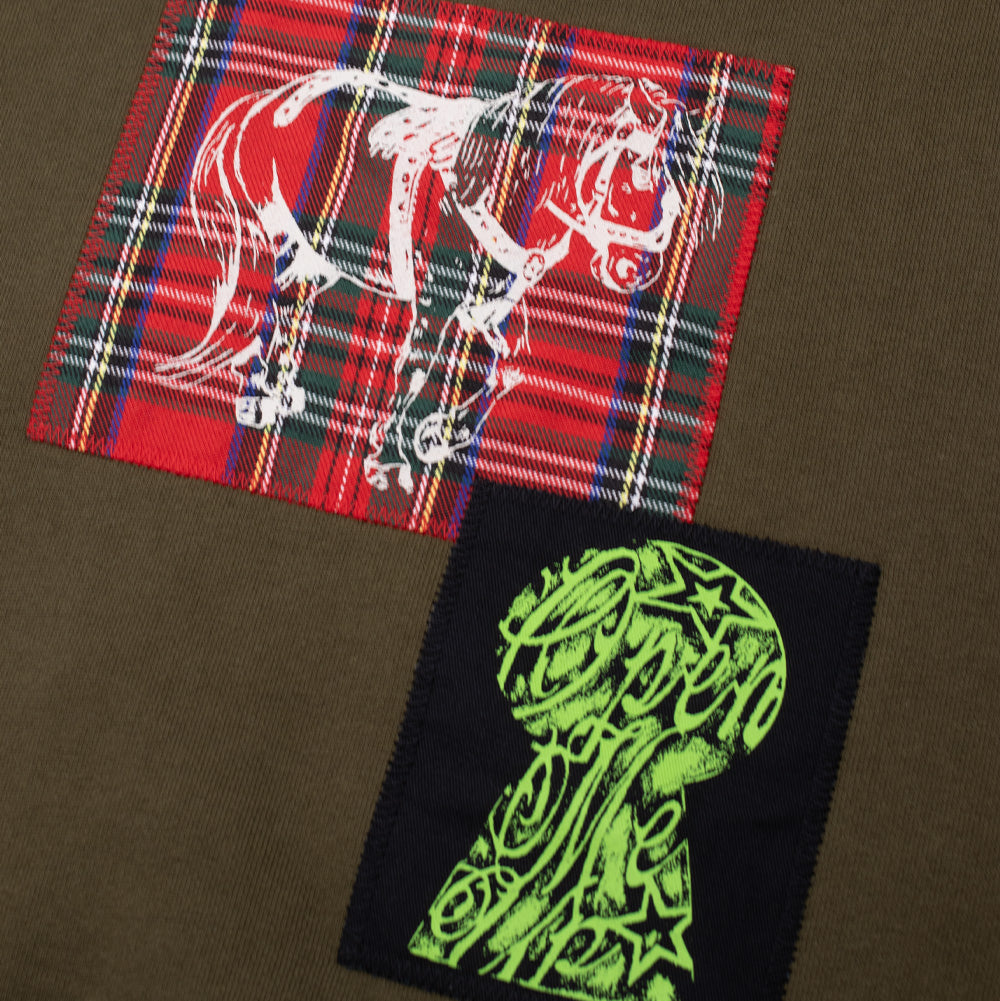 Close-up detail of the back patches on the Token Carly Zip Hoodie, showing the red woven tartan plaid patch featuring a white line art pony illustration positioned above a black patch with a neon green keyhole design.