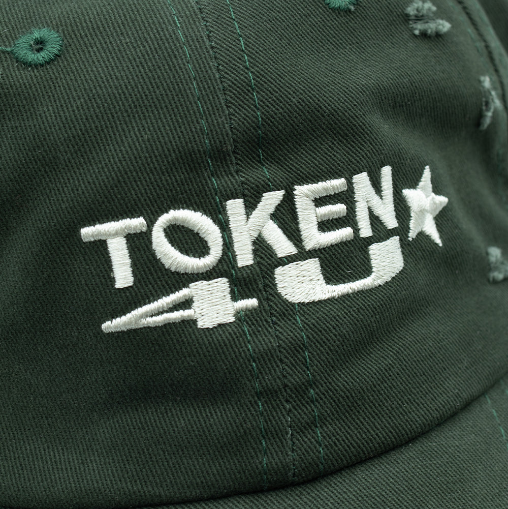 Detailed macro studio close-up of the front embroidery on the Token Lowkey Cap, focusing on the dense white satin-stitched "TOKEN 4U" logo with raised edges and star detailing, set against the dark forest green cotton fabric textured with small distressed abrasions.