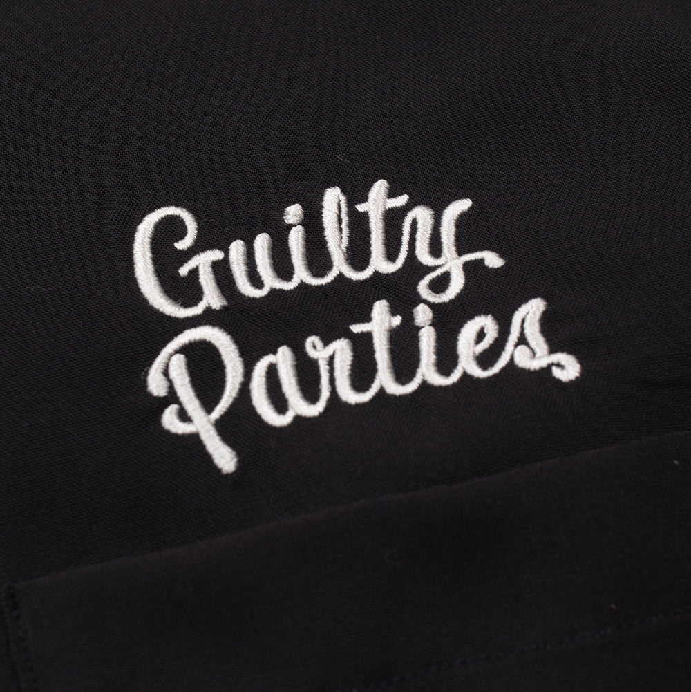 Detailed macro perspective of the chest embroidery on the Wacko Maria 50's Shirt, showcasing the dense white chain-stitched thread forming the retro two-tier "Guilty Parties" cursive lettering neatly positioned above the left chest patch pocket seam.