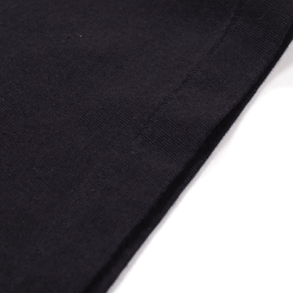 Extreme macro close-up of the bottom hem on the Wacko Maria Washed Heavy Weight Crew Neck T-Shirt, detailing the substantial knit density, washed fabric texture, and tonal parallel twin-needle stitching along the folded edge.