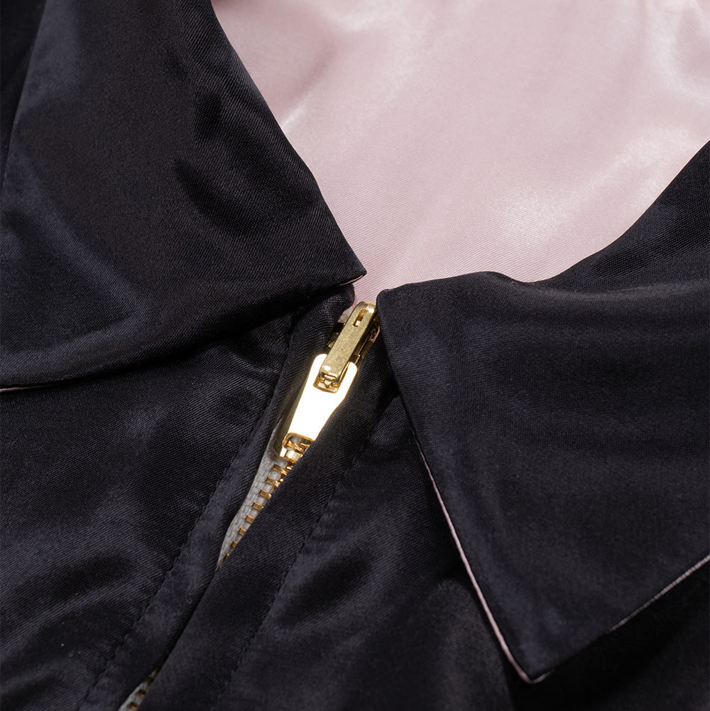 Macro studio close-up of the neckline and reversible zipper on the Wacko Maria x True Romance Ska Jacket, displaying the smooth black satin exterior folding over to reveal the soft pink inner lining, finished with a heavy-duty polished gold metal zipper slider and tracks