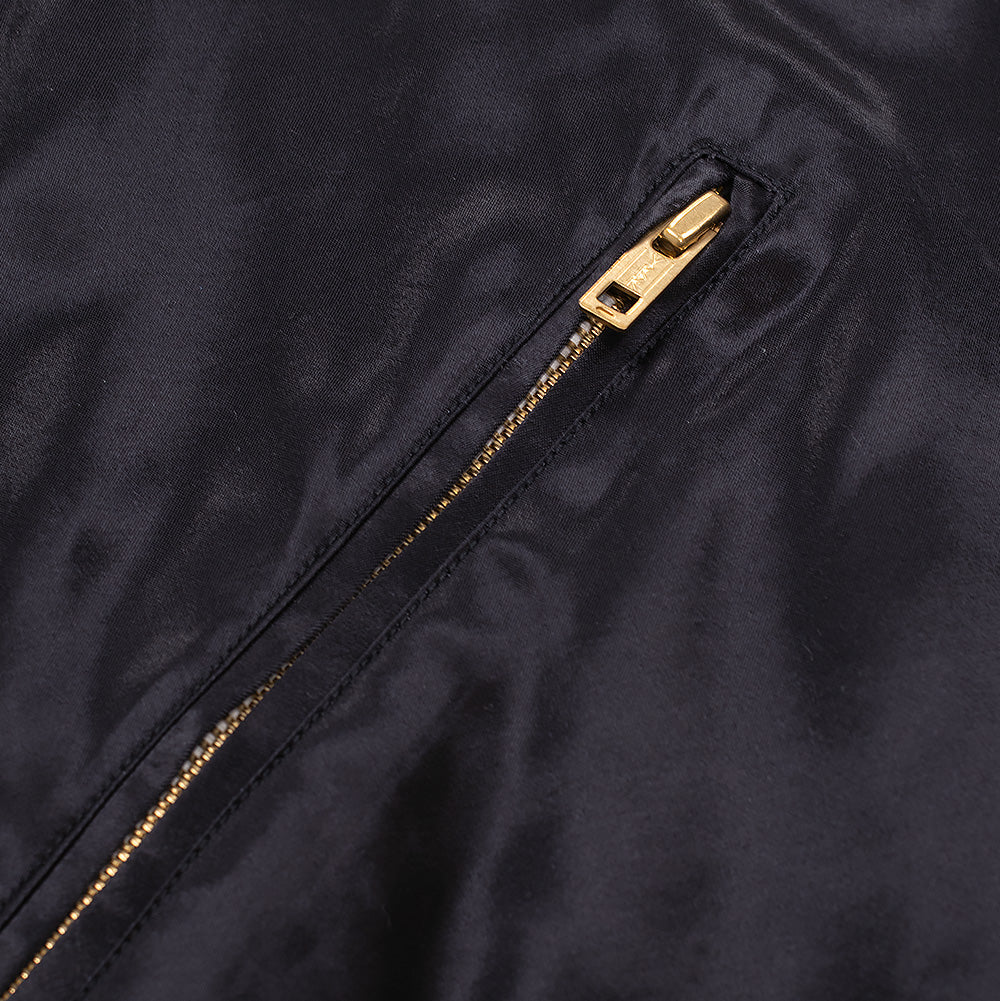 Macro close-up shot of the front waist pocket on the black side of the Wacko Maria x True Romance Ska Jacket, featuring a clean narrow welt opening secured by a shiny gold metal zipper puller against lustrous black fabric.